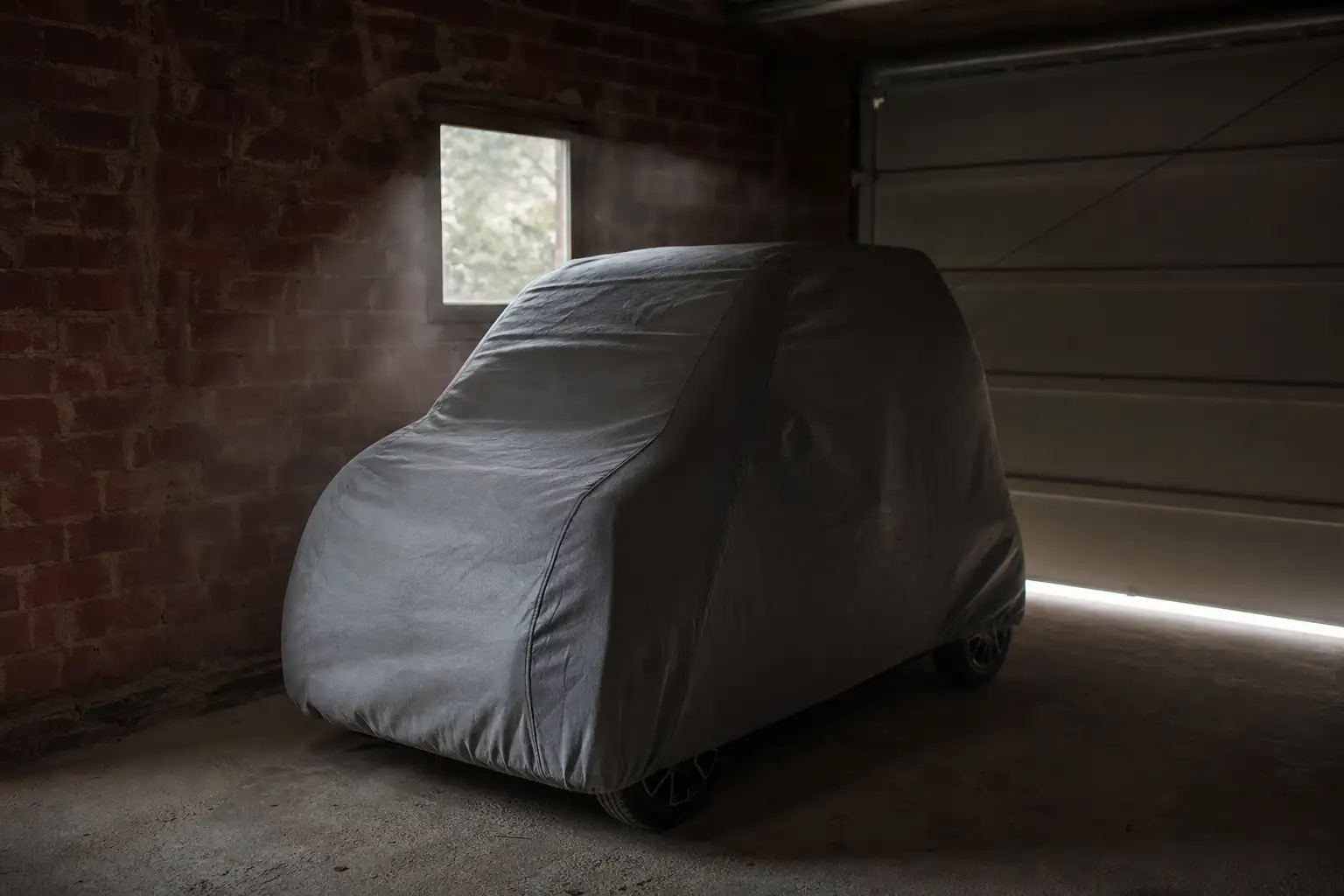 Voiture sans permis housse de protection posée sur le capot, garée dans un garage privé faiblement éclairé