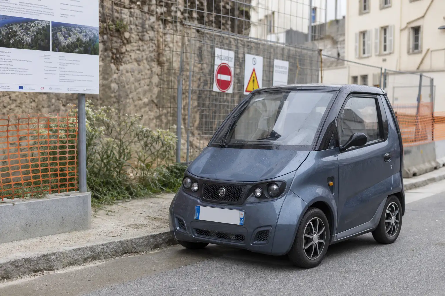 Voiture sans permis garée à proximité d'un chantier de travaux publics, panneaux de signalisation orange et barrières visibles en arrière-plan