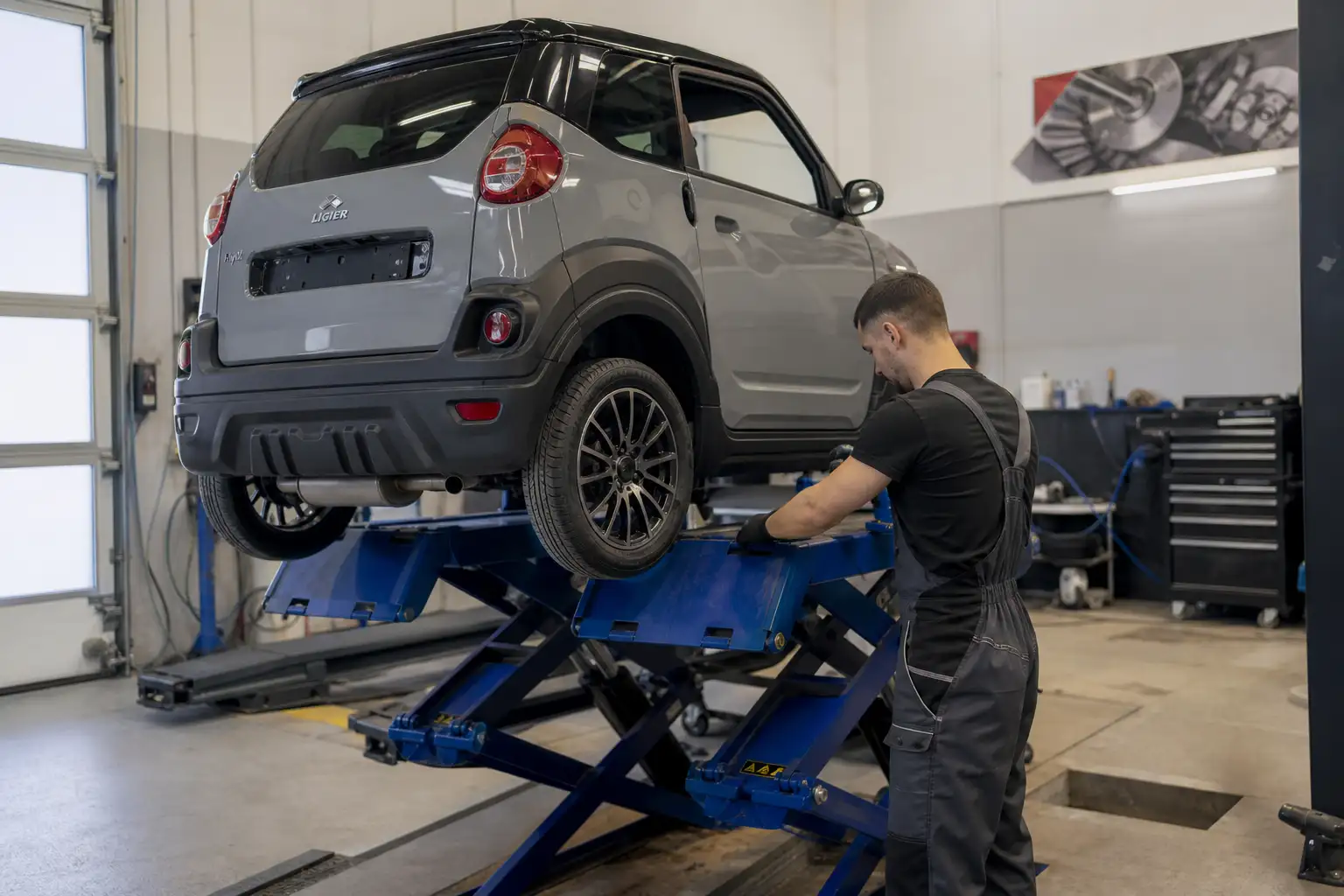 Voiture sans permis surélevée sur un pont élévateur dans un atelier de réparation automobile, mécanicien travaillant en arrière-plan, éclairage professionnel