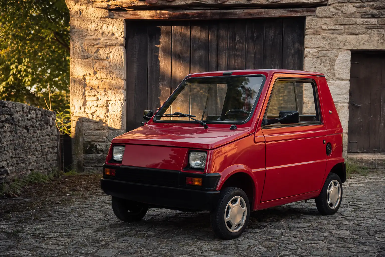 Voiture sans permis ancienne des années 1980 restaurée, garée devant un garage en pierre, ambiance patrimoine automobile