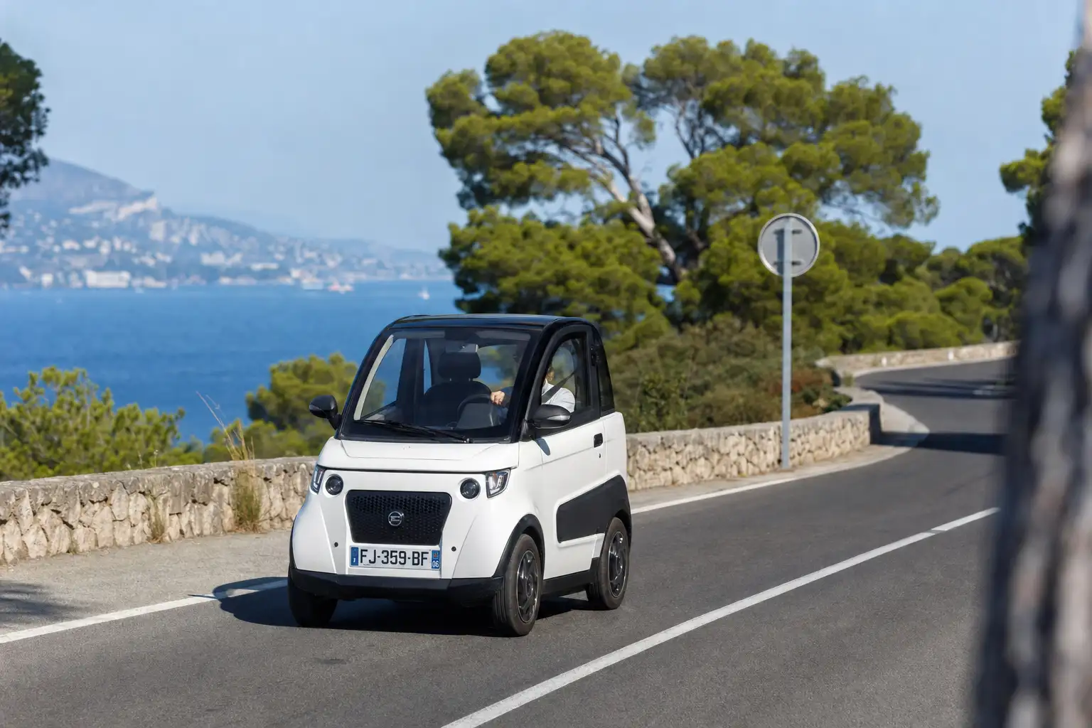 Voiture sans permis immatriculée en France roulant sur une route côtière du sud de l'Europe, panneau routier européen au bord de la chaussée