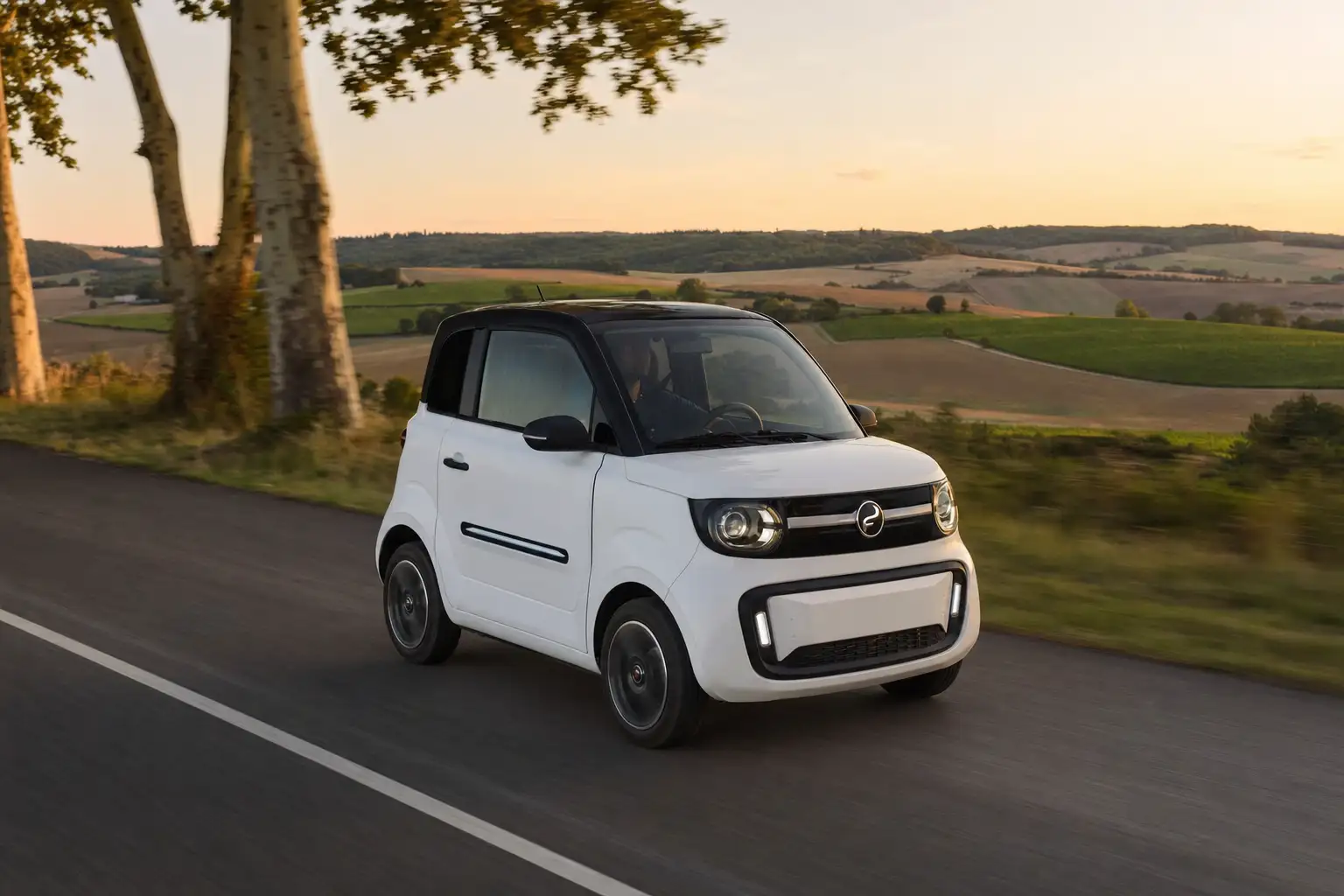 Voiture sans permis moderne roulant sur une route de campagne française au lever du soleil